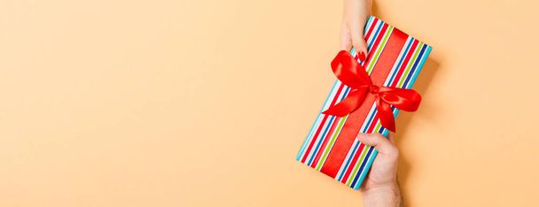 Top view of giving and receiving a present on colorful background. A man and a woman holding gift in hands. Festive concept with copy space. - Foto, Imagen