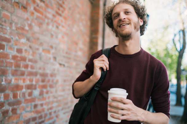 Portrait of young man walking and holding a cup of coffee outdoors on the street. Urban concept. - Photo, image