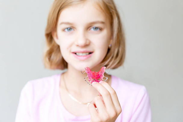 女の子はピンクの歯列矯正プレートを手に持っていて、それを示しています.  - 写真・画像