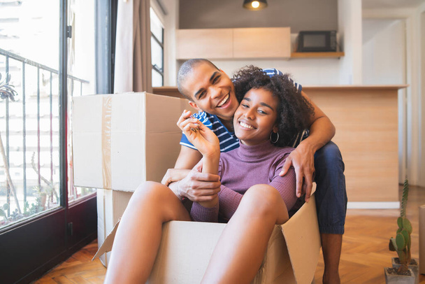 Portrait of happy latin couple having fun with cardboard boxes in new house at moving day. Real estate concept. - Photo, Image