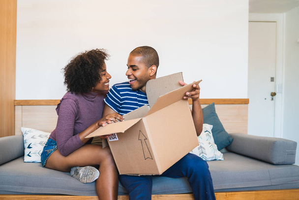Portrait of happy young latin couple opening a package at home. Delivery, shipping and postal service concept. - Photo, image