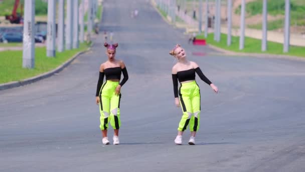 Twee jonge vrolijke vrouwen in topjes met blote schouders die dansen in vrije stijl straatdansen, hiphop choreografie op een brede straat. Langzame beweging - Video