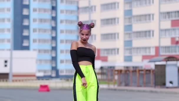 Young beautiful woman in top with bare shoulders dancing modern youth dance with twerking elements outdoors against the background of the building. Slow motion - Footage, Video