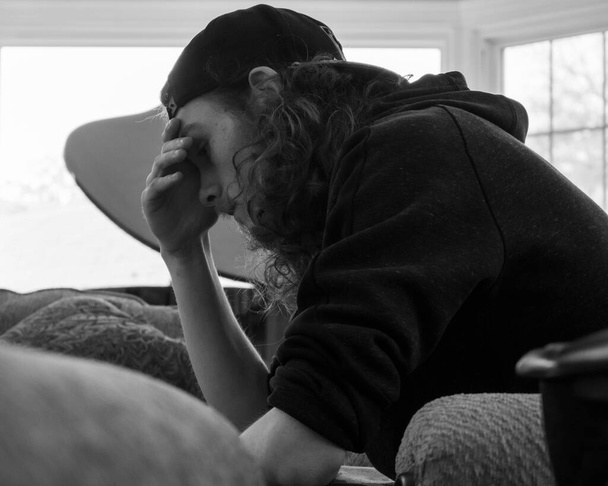 Een zwart-wit shot van een gestreste en verontruste jonge man met een hoed - Foto, afbeelding