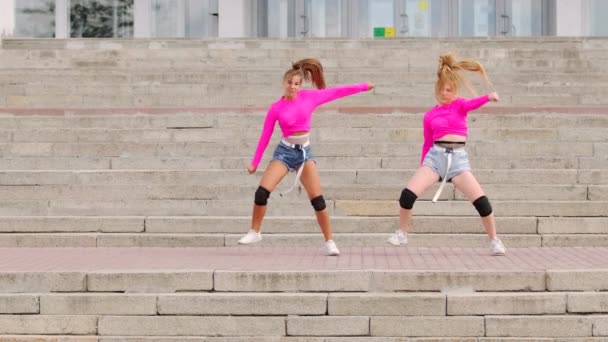 Twee mooie jonge meisjes in korte shorts dansen gratis straatdansen, hiphop choreografie op een enorme stenen trap. Langzame beweging - Video