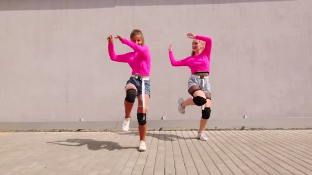 Dwie wesołe młode dziewczyny w krótkich spodenkach tańczące hip hop, wykonuje spektakularne elementy współczesnej młodzieży taniec pod ścianą. Zwolniony ruch - Materiał filmowy, wideo
