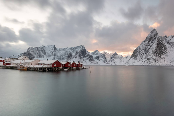 Τοπίο των νησιών Lofoten στη Νορβηγία με παραδοσιακές ξύλινες, κόκκινες καλύβες ψαράδων μπροστά στη θάλασσα και αυτό το όμορφο βουνό στο βάθος. Προορισμός χειμερινών ταξιδιών. - Φωτογραφία, εικόνα