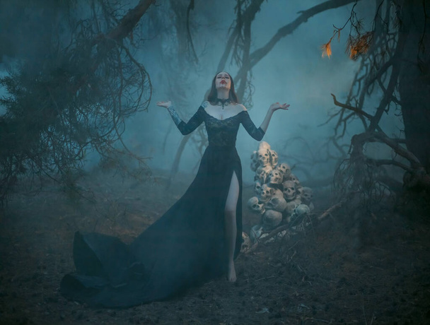 Blurred silhouette of mystical pagan woman in the fog. The witch casts a spell, prays in the forest with her hands raised to the sky against the background of a dark tree and human skulls - Φωτογραφία, εικόνα