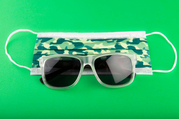 Maschera chirurgica camo e occhiali da sole su sfondo verde - Foto, immagini