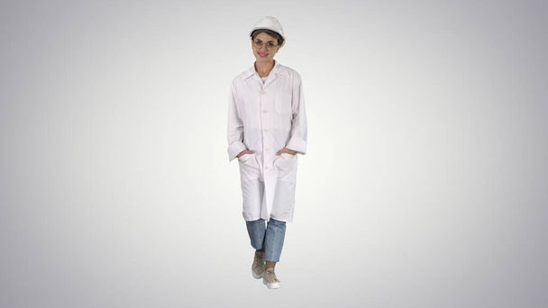 Woman in a gradient lab coat and hard hat walking on gradient ba - Foto, afbeelding