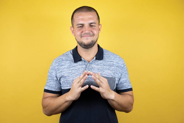 Russian man standing over insolated yellow background with Hands together and fingers crossed smiling relaxed and cheerful. Success and optimistic - Photo, Image