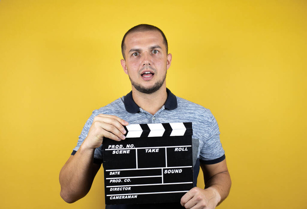 Russian man standing over insolated yellow background standing over isolated yellow background holding clapperboard very happy - Photo, Image