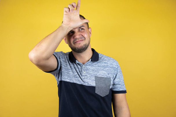 Російський чоловік, що стоїть над інсольованим жовтим фоном, сміється з людей з пальцями на лобі, глузує і ображає.. - Фото, зображення