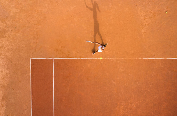 Gesunder Lebensstil. Ein junges Mädchen spielt auf dem Platz Tennis. Der Blick aus der Luft auf den Tennisspieler. Schmutzgericht. Sportlicher Hintergrund. Luftaufnahme von der Drohne.  - Foto, Bild
