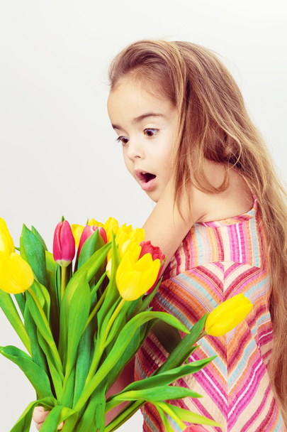Surprised little girl with bouquet of tulips - Фото, зображення