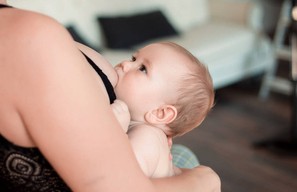 A young mother is breastfeeding her little child and looking at him tenderly - 写真・画像