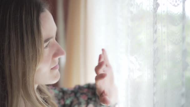 Dívka jemně kartáče rukou přes krajkové záclony při pohledu z okna, zavřít - Záběry, video