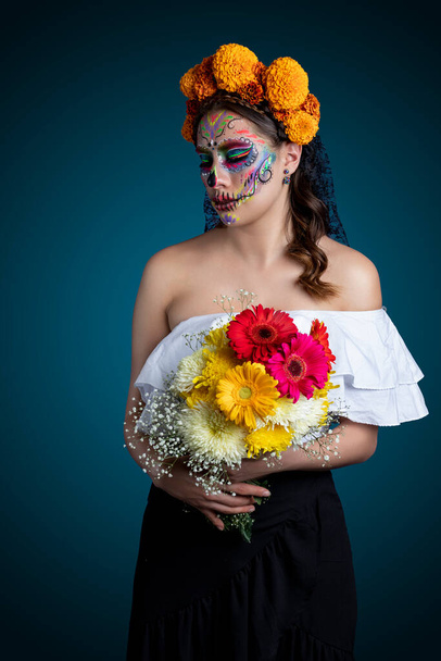 Lateinische Frau mit Catrina Make-up und einem Blumenstrauß in ihren Händen - Foto, Bild
