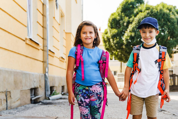 Front view portrait of small caucasian boy and girl brother and sister or little friends children going to school first grade pupils with backpack bags on their back in sunny day outdoor copy space - Photo, Image