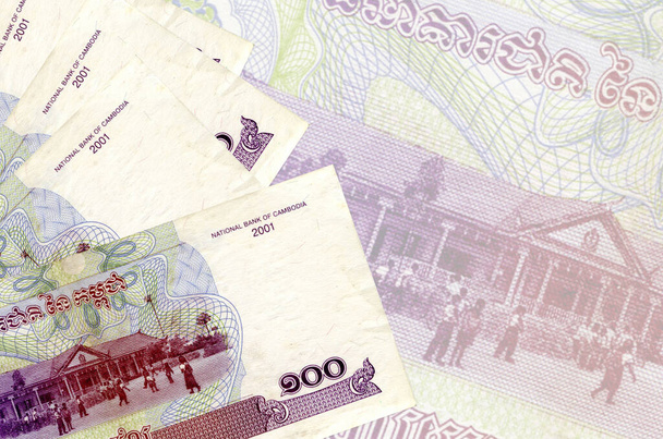 100 Cambodjaanse riels biljetten liggen in stapel op de achtergrond van grote semi-transparante bankbiljet. Abstract zakelijke achtergrond met kopieerruimte - Foto, afbeelding