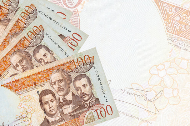 Τα χαρτονομίσματα των 100 Δομινικανών πέσο βρίσκονται σε στοίβα στο φόντο ενός μεγάλου ημι-διαφανούς τραπεζογραμματίου. Αφηρημένο επιχειρηματικό υπόβαθρο με αντίγραφο χώρου - Φωτογραφία, εικόνα