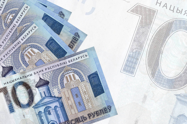 10 weißrussische Rubel-Scheine liegen gestapelt auf dem Hintergrund einer großen halbtransparenten Banknote. Abstrakter geschäftlicher Hintergrund mit Kopierraum - Foto, Bild