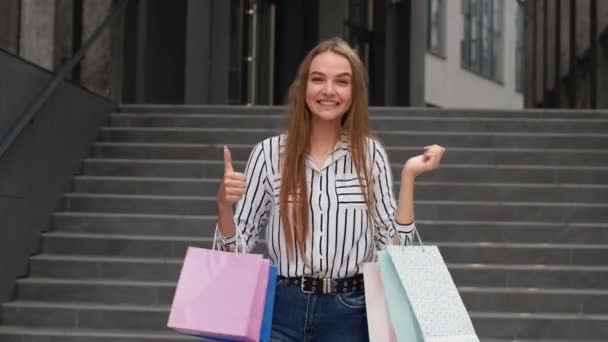 スタイリッシュな女の子を保持ショッピングバッグと親指を表示。良い休日の販売の割引で楽しむ - 映像、動画