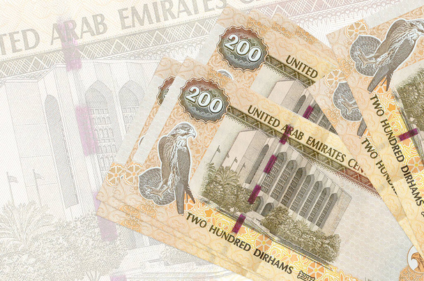 200 купюр дирхамов ОАЭ лежат в стопке на фоне большой полупрозрачной купюры. Абстрактное представление национальной валюты. Концепция бизнеса - Фото, изображение