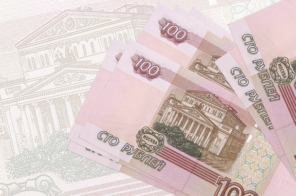 Τα χαρτονομίσματα των 100 ρουβλίων της Ρωσίας βρίσκονται σε στοίβα στο φόντο ενός μεγάλου ημι-διαφανούς τραπεζογραμματίου. Περίληψη της παρουσίασης του εθνικού νομίσματος. Επιχειρηματική έννοια - Φωτογραφία, εικόνα