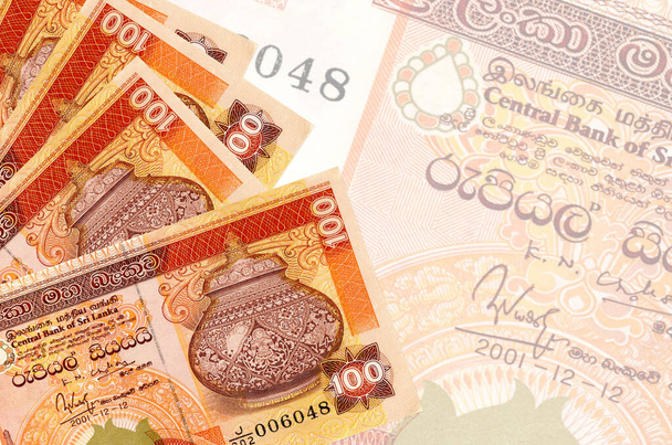 100 Sri Lankaanse roepies biljetten liggen in stapel op de achtergrond van grote semi-transparante bankbiljet. Abstract zakelijke achtergrond met kopieerruimte - Foto, afbeelding