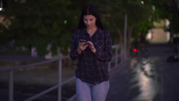 Mujer sonriente usando el teléfono en la calle, mirando la pantalla, mensajes de texto de chat en línea - Metraje, vídeo