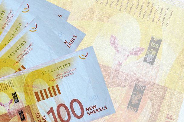 100 nouveaux billets israéliens en shekels sont empilés sur fond de gros billets semi-transparents. Fond d'entreprise abstrait avec espace de copie - Photo, image