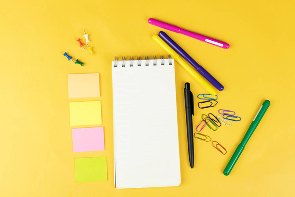 Top view of blank notebook and school supplies like colored markers, sticker and clipers on yellow background, space for text - Fotografie, Obrázek