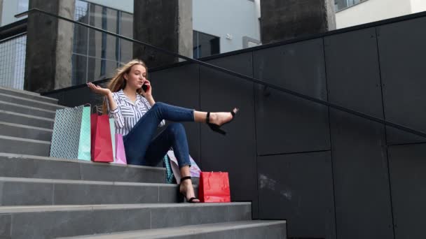 Κορίτσι κάθεται στις σκάλες με τσάντες μιλώντας στο smartphone για την πώληση στο εμπορικό κέντρο στη Μαύρη Παρασκευή - Πλάνα, βίντεο