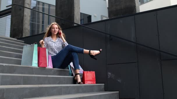 Meisje zit op de trap met tassen praten op mobiele telefoon over de verkoop in het winkelcentrum in Black Friday - Video
