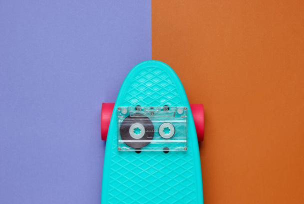 Pop art retro style still life. 80s. Cruiser board with audio cassette on a two-color paper background. Top view. - Fotografie, Obrázek