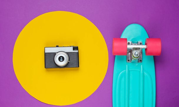 Cruiser board and retro film camera on purple background with a yellow circle. Summer fun. Studio fashion shot. 80s, pop culture. Top view. - Photo, Image