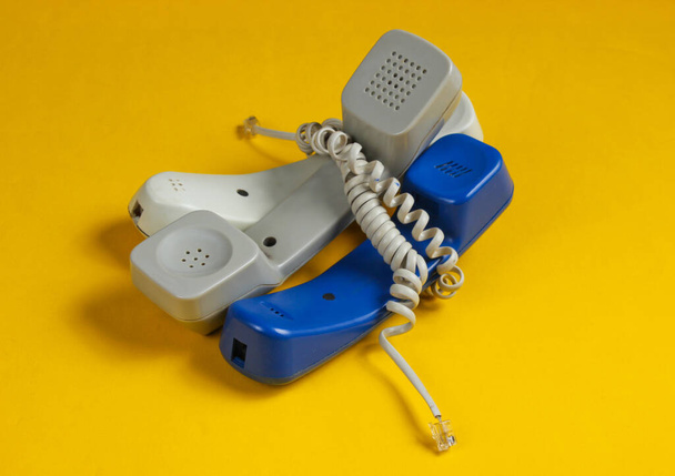 Trois tubes de téléphone de bureau enveloppés dans le câble sur fond bleu studio. Call center, concept de hotline - Photo, image