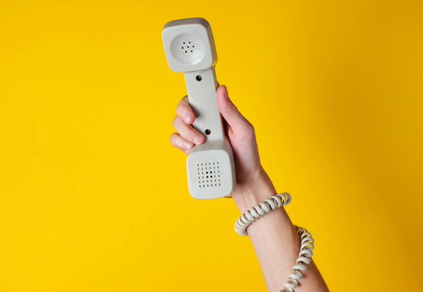 Nainen käsi kääritty kaapeli pitää puhelin putki keltaista taustaa vasten. Satamataidetta Luova minimalismi. Yläkuva - Valokuva, kuva
