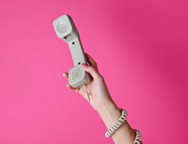 Vrouwelijke hand verpakt in kabel houdt telefoon buis tegen roze achtergrond. Havenkunst. Creatief minimalisme. Bovenaanzicht - Foto, afbeelding