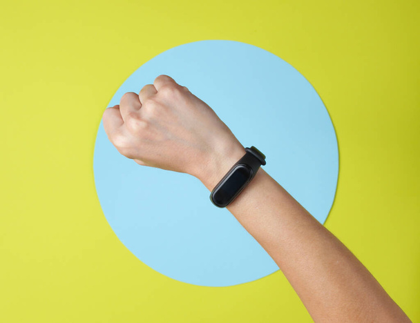 Smart bracelet on hand wrist on green background with blue circle. Top view - 写真・画像