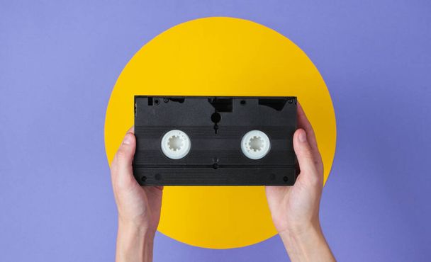 Femmina mano tenendo videocassetta su sfondo viola con cerchio giallo - Foto, immagini