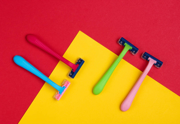 Plastic colored razors on a red-yellow background. Minimalistic fashion concept. Top view - Foto, Imagen