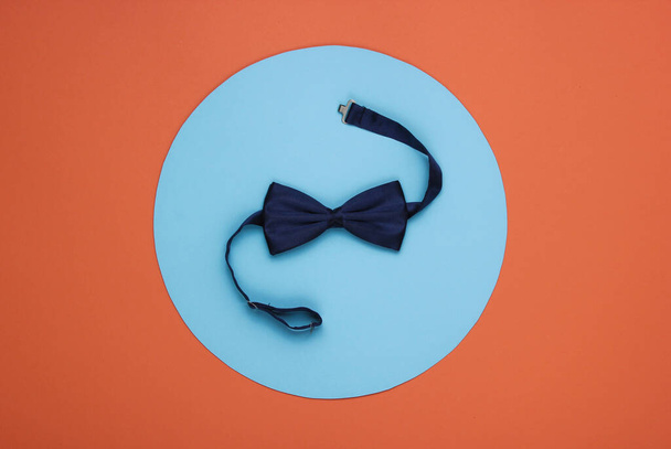 Bow stropdas op koraal papier achtergrond met blauwe cirkel in het midden. Bovenaanzicht. - Foto, afbeelding