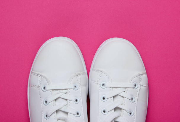 Κομψά λευκά sneakers σε ροζ χάρτινο φόντο με ροζ κύκλο. Μινιμαλιστική έννοια μόδας. Άνω όψη - Φωτογραφία, εικόνα
