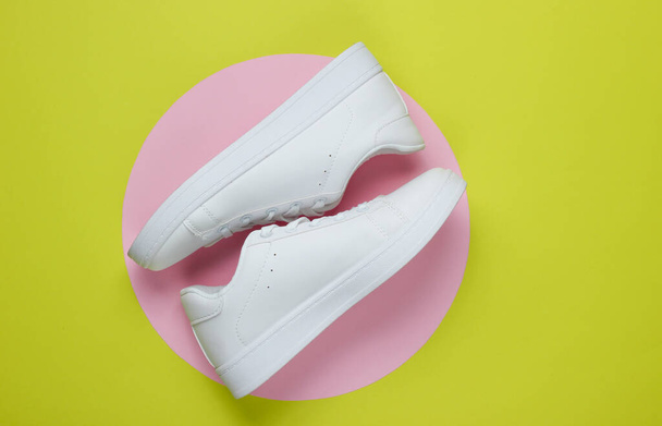 Elegantes zapatillas blancas sobre fondo de papel verde con círculo de pastel rosa. Concepto de moda minimalista. Vista superior - Foto, imagen