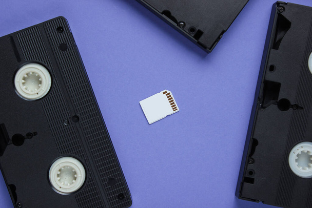 Carte mémoire SD, cassette vidéo sur fond de papier violet. Stockage moderne et obsolète pour les supports. Vue du dessus - Photo, image