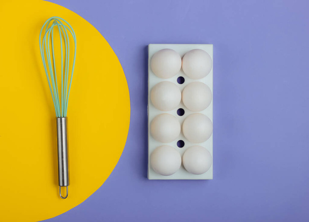 Tray with white chicken eggs and whisk on blue background. Minimalistic food concept. - Valokuva, kuva