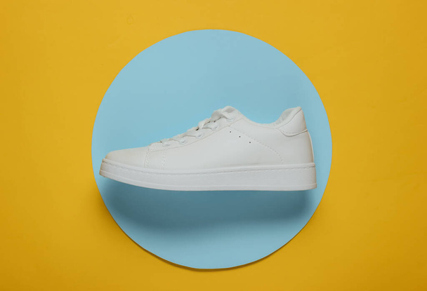Stylish white sneaker on a yellow background with blue circle in the middle. Top view. Minimalism fashion still life - Photo, Image