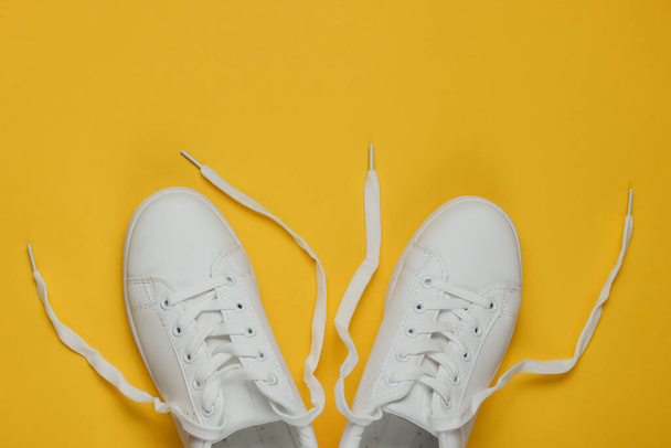 Stylish white sneakers with untied laces on a yellow background. Top view - Fotografie, Obrázek